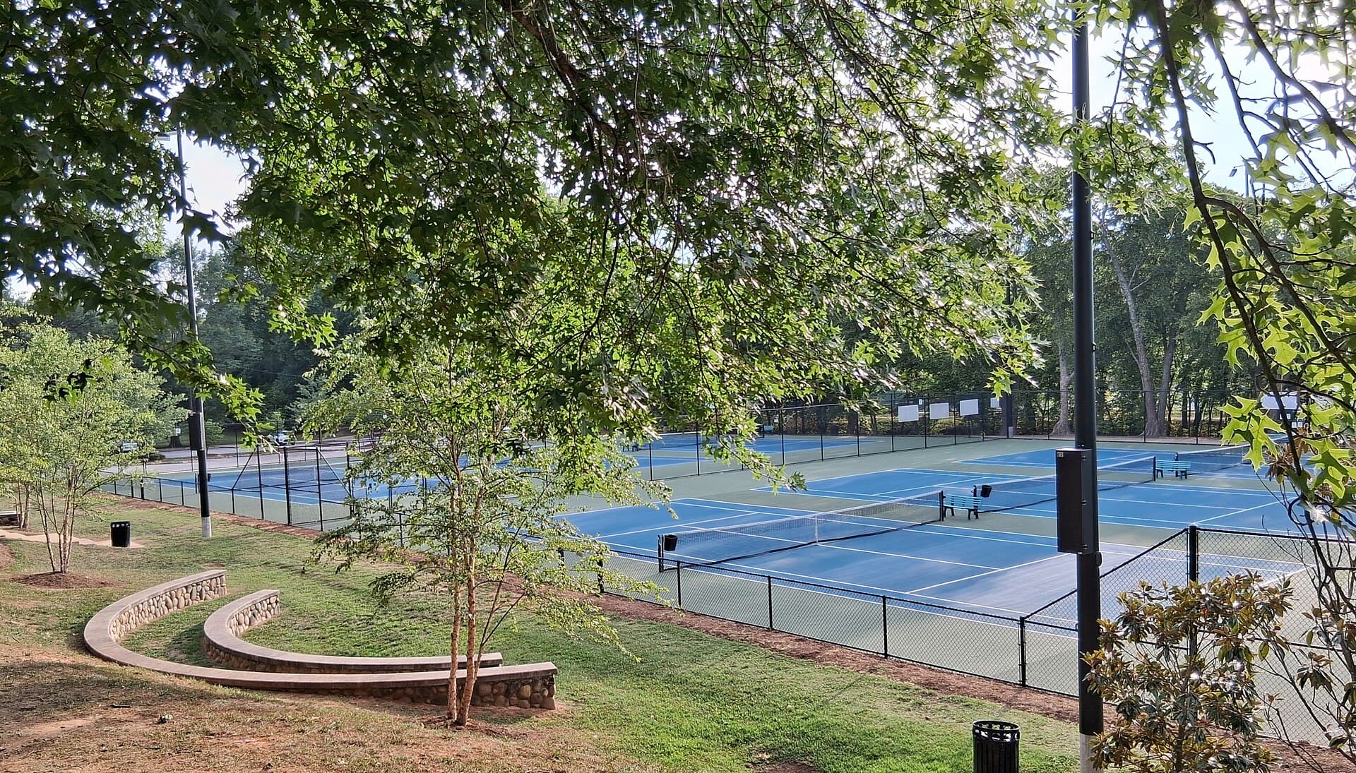 Blue hard tennis courts seen through trees