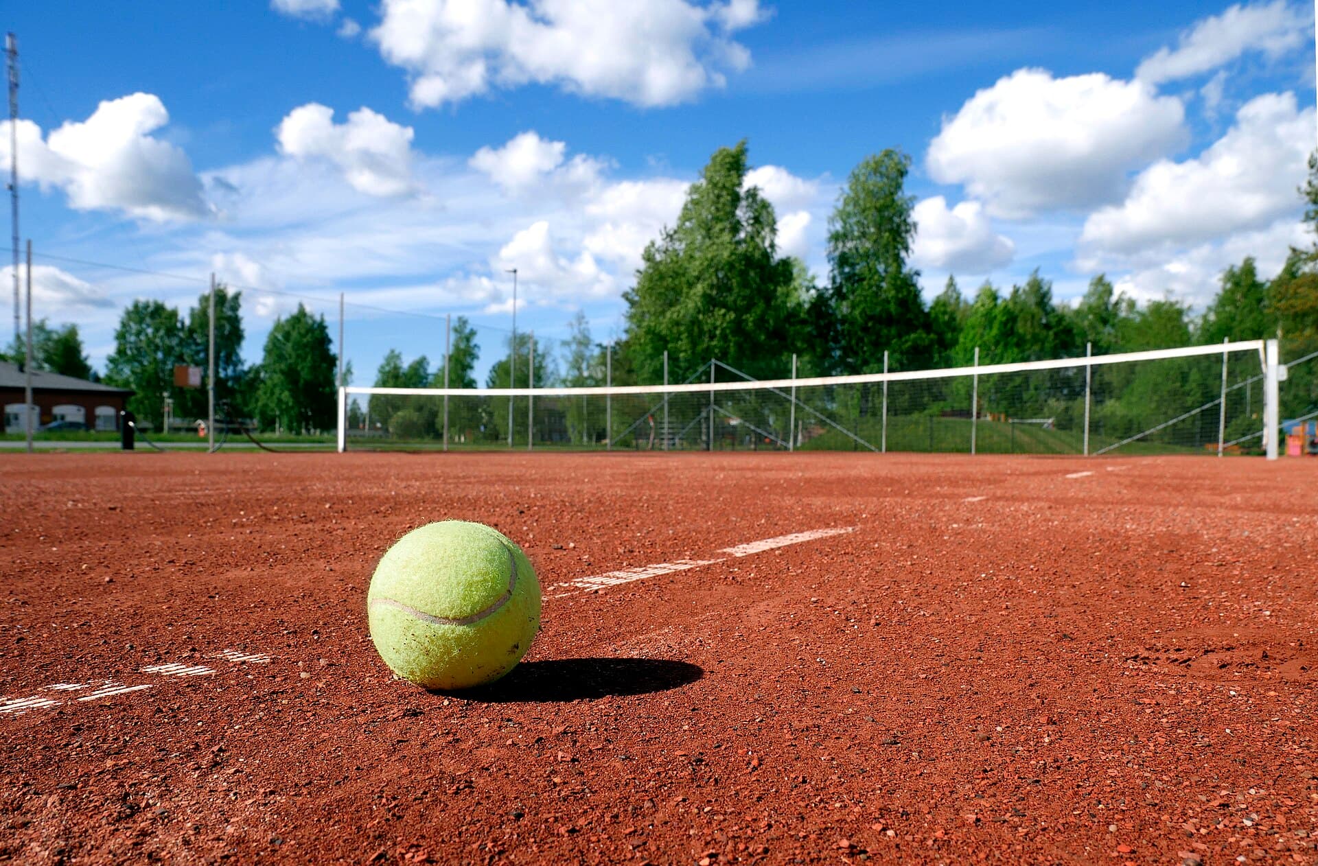 A yellow tennis ball resting on a clay court in front of the net